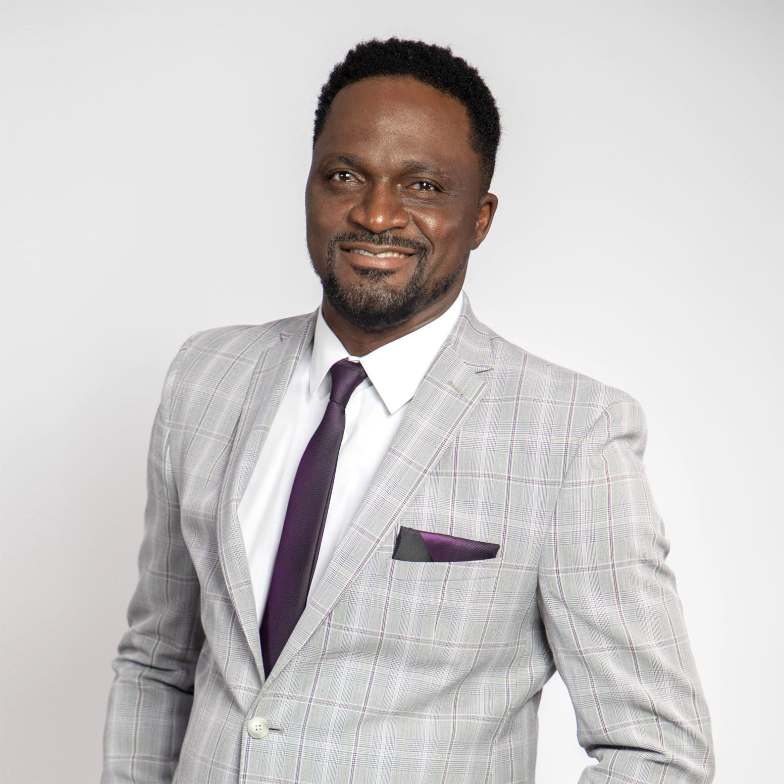 Kingdom Revealed - Pastor Saa, smiling at you, wearing in a grey suit with a purple tie.